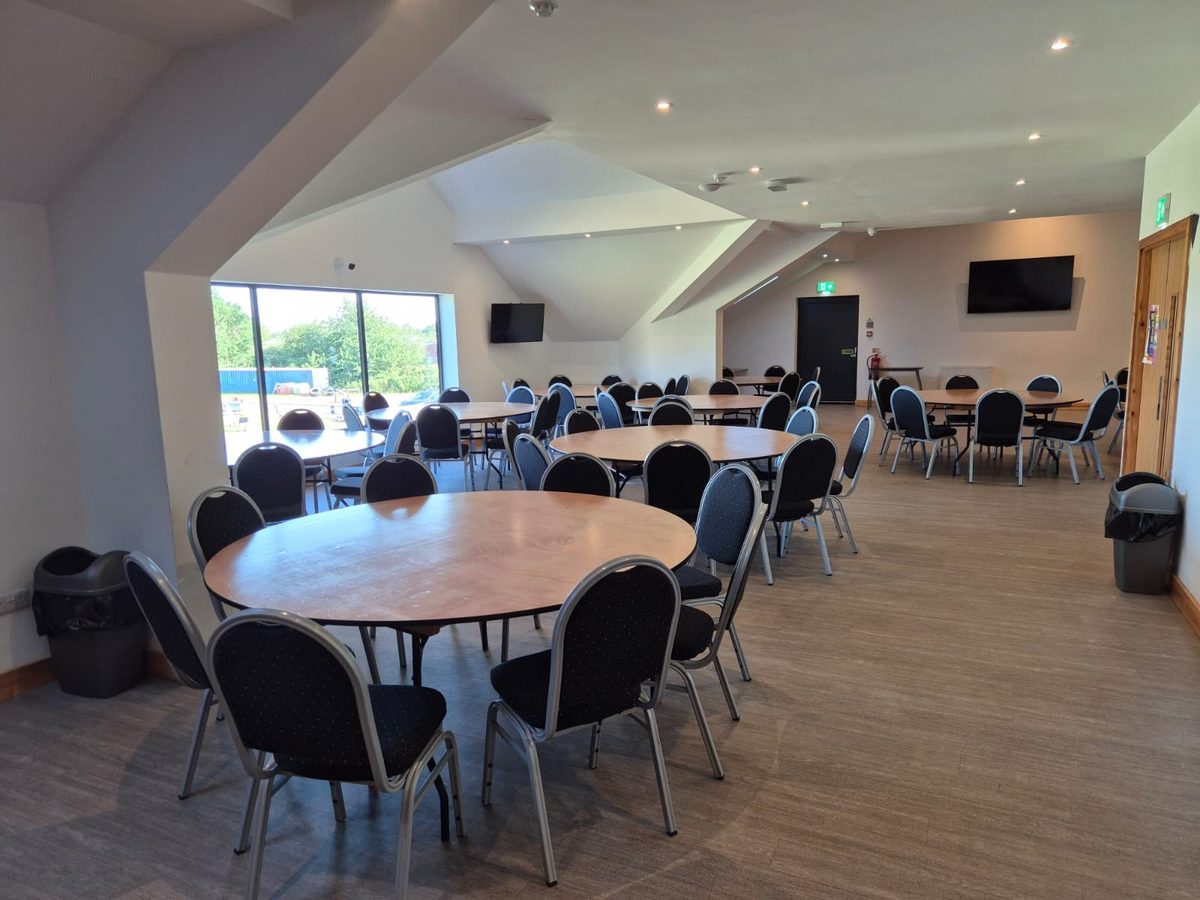 Another view of the function room set up with round tables, screens and large windows overlooking the pitch