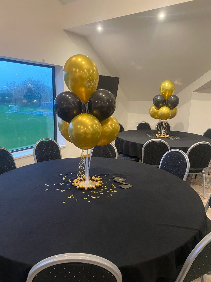 A table set with a balloon centrepiece, confetti and favours, with the pitch visible through the window behind